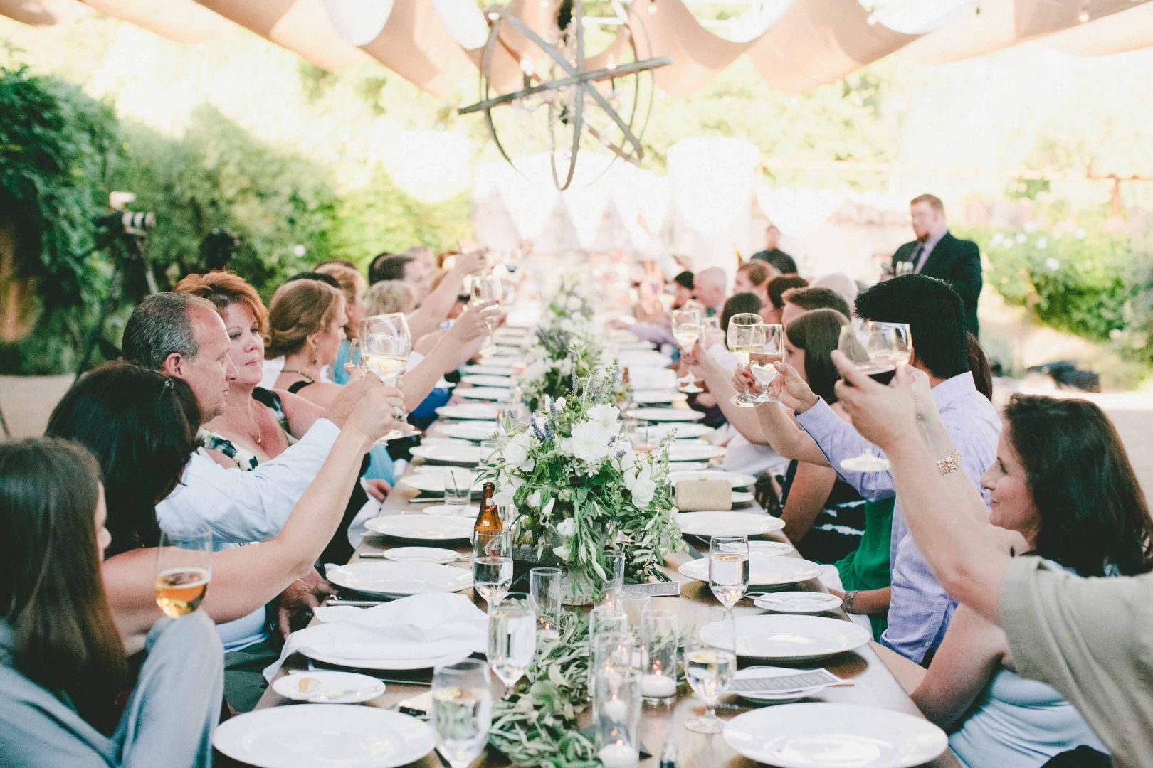 people toasting with wine in a super long table served with plates waiting for the food